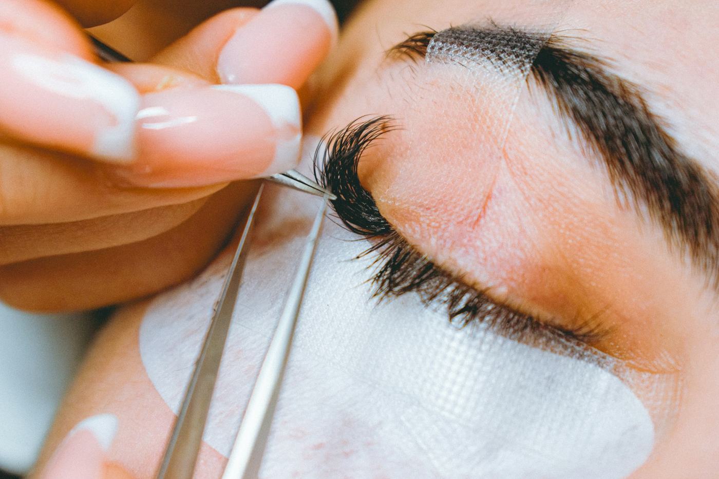 Lash designer aplicando extensão de cílios com duas pinças, com protetor sob os olhos